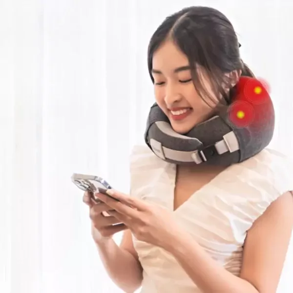 Woman smiling, wearing a neck massager and looking at her phone.