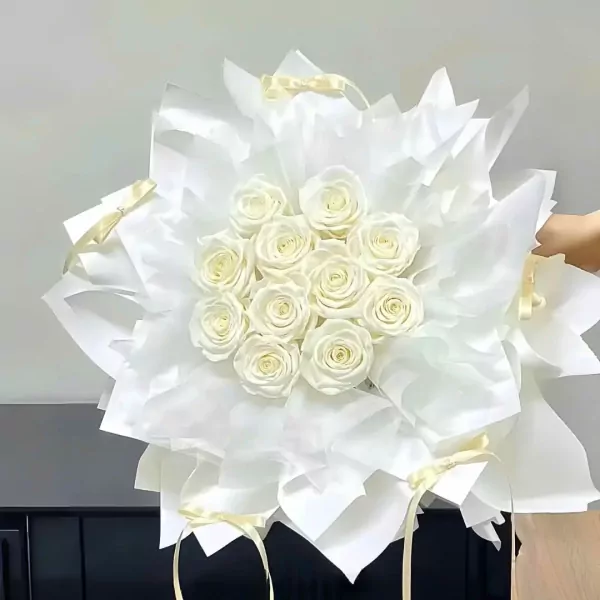 White roses arranged in a bouquet with white wrapping paper and yellow ribbons.