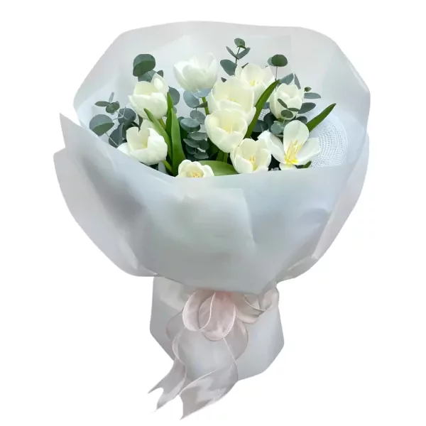 White tulips and eucalyptus in a white paper bouquet with a pink ribbon.