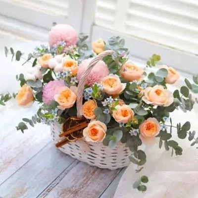 White basket with pink and orange roses, eucalyptus, and small blue flowers.