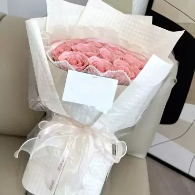 A bouquet of pink roses wrapped in white paper and tied with a white ribbon.