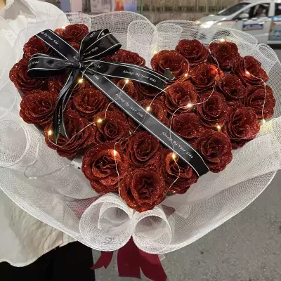 Glittering red roses arranged in a heart shape with a black ribbon and fairy lights.