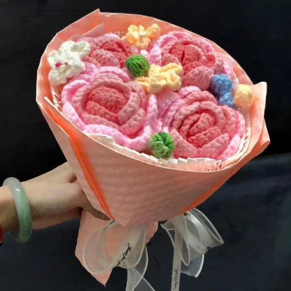 Hand holding a pink knitted rose bouquet with white ribbon.
