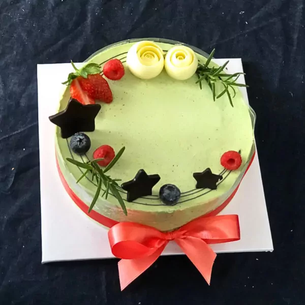 Green matcha yogurt mousse cake with strawberries, blueberries, raspberries, chocolate stars, and white rosettes.