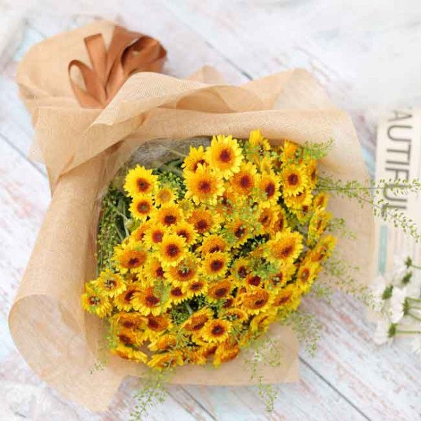 Bright yellow sunflowers in a bouquet wrapped in brown paper, tied with a ribbon.