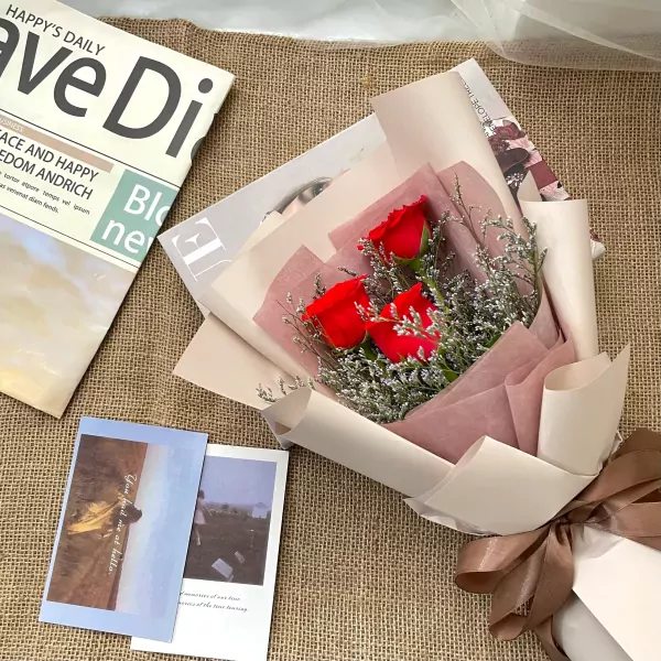 Bouquet of three red roses, wrapped in pale pink and cream paper, with a brown ribbon.