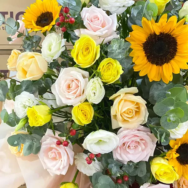 Bright sunflower and rose bouquet with eucalyptus leaves and berries.