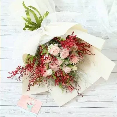 A bouquet of pink roses and red orchids, wrapped in white paper with a white ribbon.