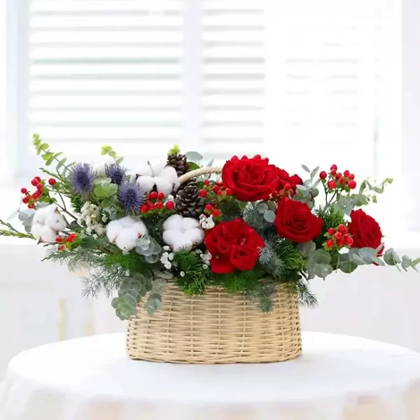 Basket of red roses, cotton, pinecones, and berries with eucalyptus and thistle.