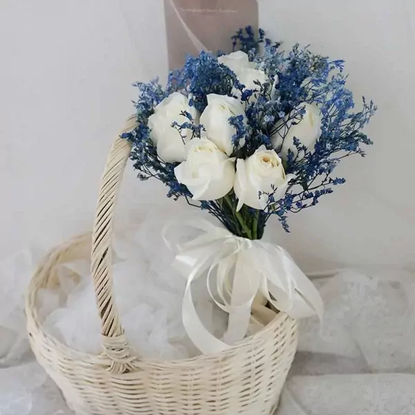 White roses with blue accents in a basket, tied with a white ribbon.