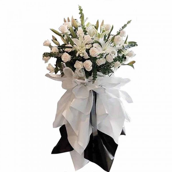 White lilies and roses in a funeral arrangement with white and black fabric.