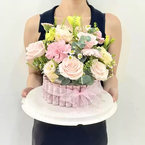 Pink floral arrangement on a money cake box, held by a person.