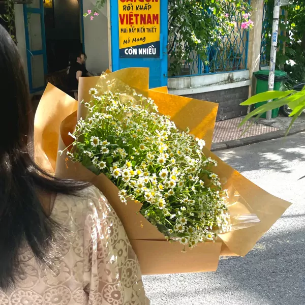Woman holding a bouquet of Tana daisies wrapped in brown paper.