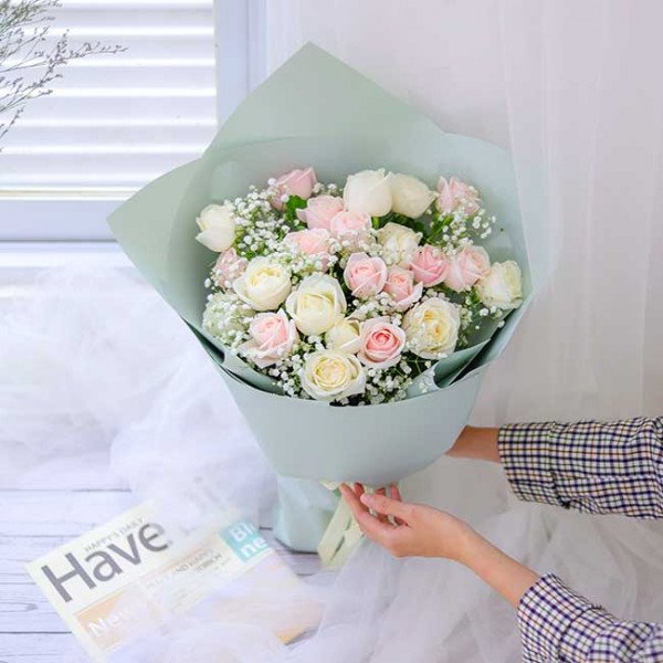 Bouquet of pink and white roses with baby's breath, wrapped in pale green paper.