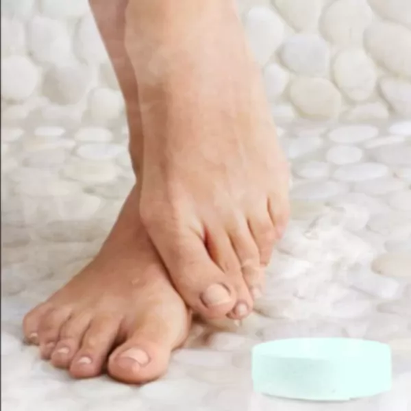 Feet resting on a pebble shower floor with a bath bomb.