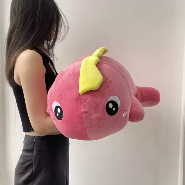 A person holds a large, pink, plush dinosaur toy with big eyes and a yellow tail.