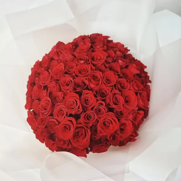 A large bouquet of 99 red roses, beautifully arranged and wrapped in white paper.