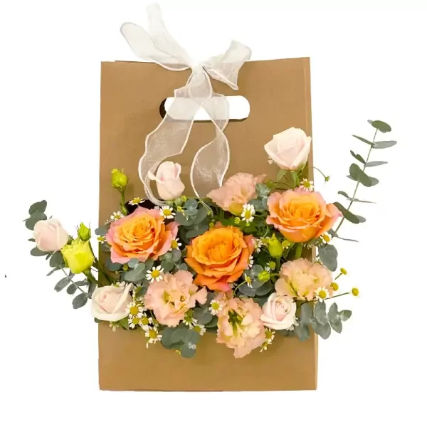 Gift bag with orange roses, lisianthus, and accent flowers, tied with white ribbon.