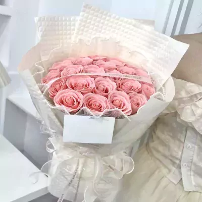 A glamorous bouquet of pink roses wrapped in white paper and tied with a ribbon.