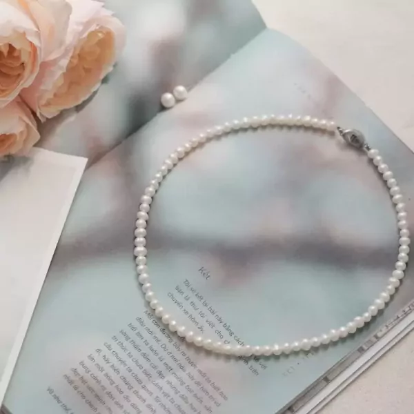 A delicate pearl necklace lies on a book, with pink roses nearby.