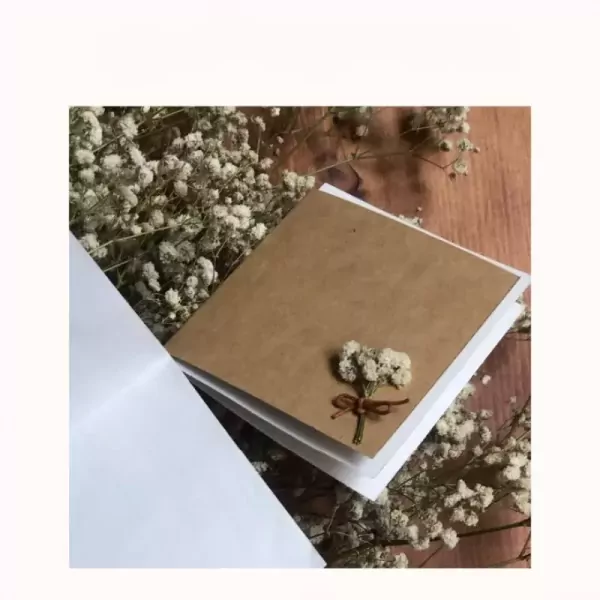 A kraft paper card with dried flowers tied with twine sits on a bed of baby's breath.