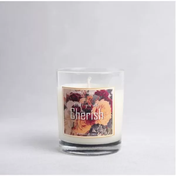 A glass-encased scented candle with a floral label that reads "Cherish".