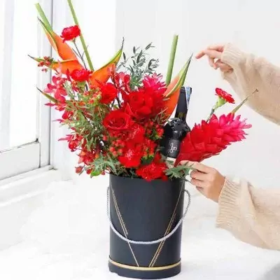 Red flowers with a bottle of red wine in a black vase with gold accents.