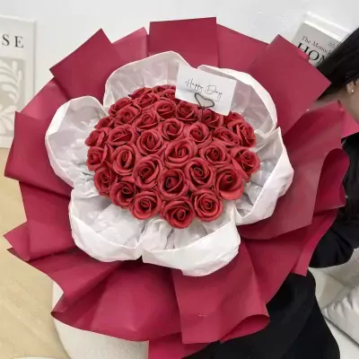 A bouquet of red roses, artfully arranged with white and deep red wrapping.