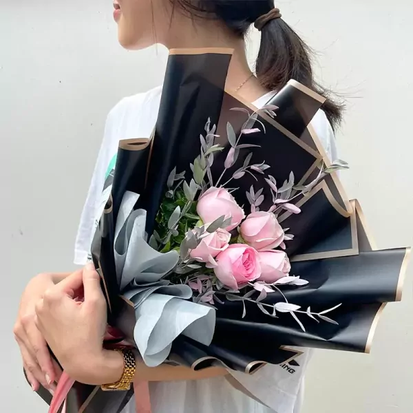 A bouquet of pink roses with black and gold wrapping.