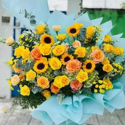 Bouquet of yellow and orange roses and sunflowers with blue paper wrapping.