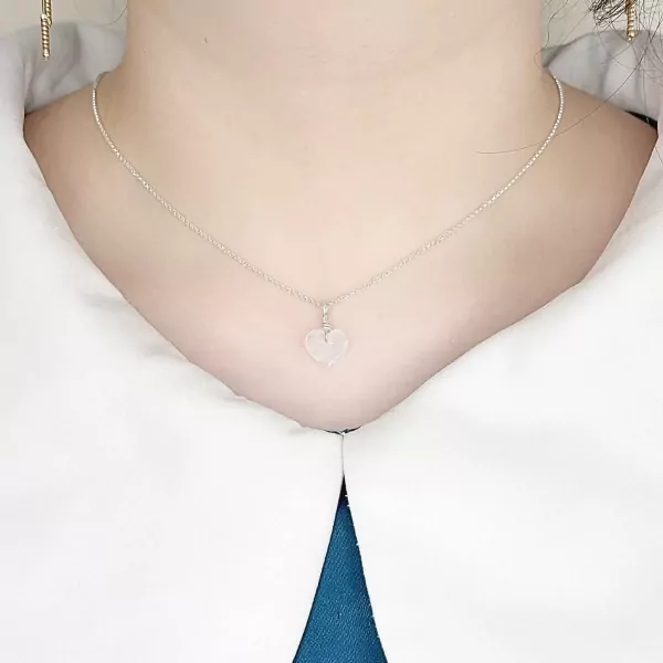 Silver necklace with a clear quartz heart pendant on a person's neck.