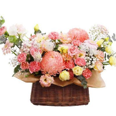 Pink and yellow flowers in a brown woven basket, including chrysanthemums, carnations, and asters.