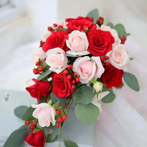 Red and pale pink roses with red berries and eucalyptus leaves in a cascading bouquet.