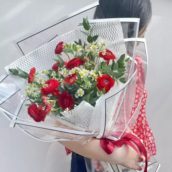 Red ranunculus and white tana flowers in a clear bouquet wrap with a red ribbon.