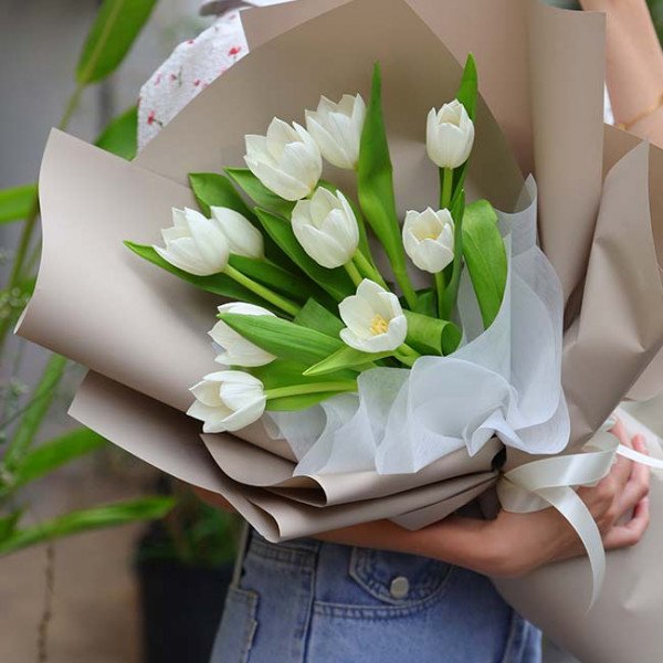 Bouquet of white tulips wrapped in brown paper with white tulle and ribbon.