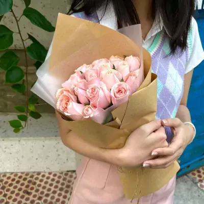 A bouquet of 22 pink roses wrapped in brown paper, held by a person wearing a sweater vest.