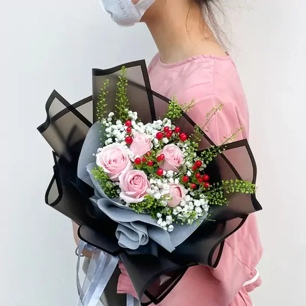 Bouquet of pink roses, baby's breath, and red berries with black and gray wrapping.