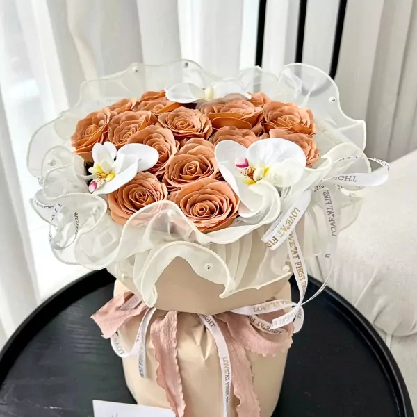 Peach roses and white orchids in a flowing sheer fabric wrap, tied with ribbon.