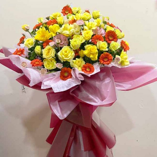 Bright yellow roses and orange gerbera daisies in a large pink floral arrangement.