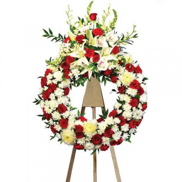 Funeral wreath with red roses, white and yellow chrysanthemums, lilies, and other greenery on a stand.