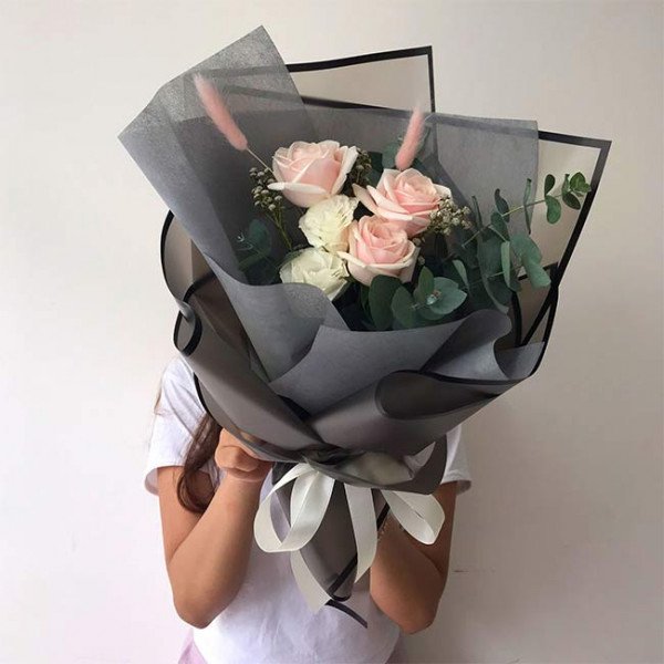 Bouquet of pink and white roses with eucalyptus in dark grey paper, tied with a white ribbon.
