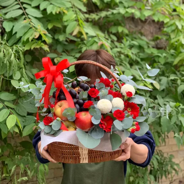 Fruit and flower basket with apples, grapes, red gerbera daisies, and white chrysanthemums.