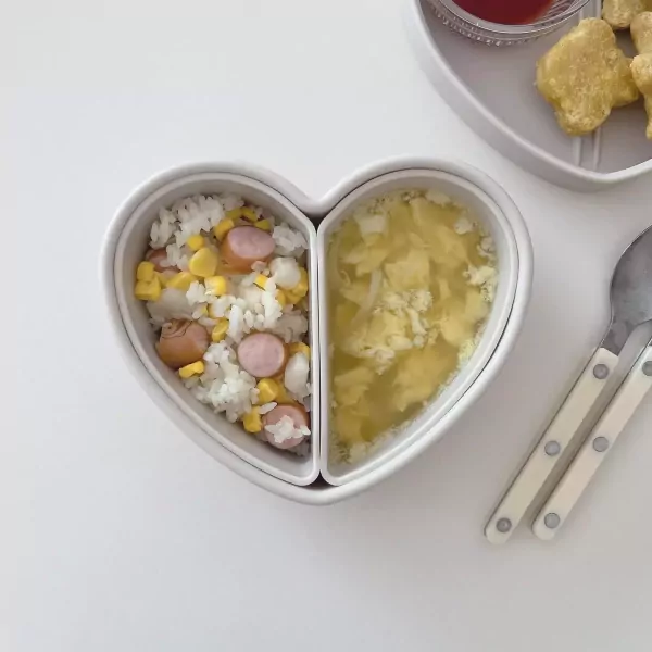 Heart-shaped lunchbox with rice, corn, sausage, and soup.