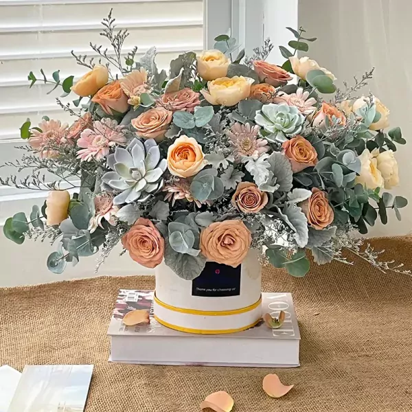 Elegant floral box with peach and pink roses, succulents, and greenery.