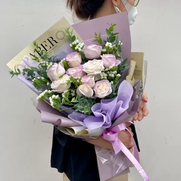 A person holds a bouquet of light purple and white roses with eucalyptus leaves.