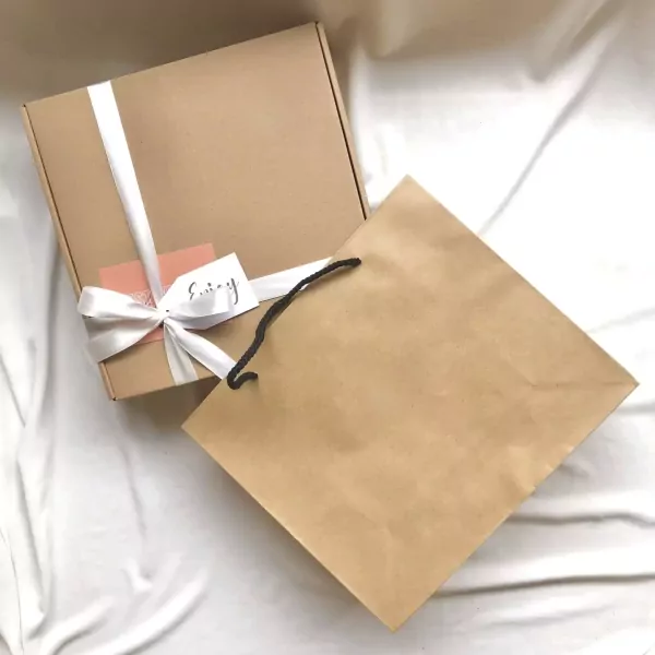 A brown gift box with white ribbon and a small tag, next to a brown paper gift bag.