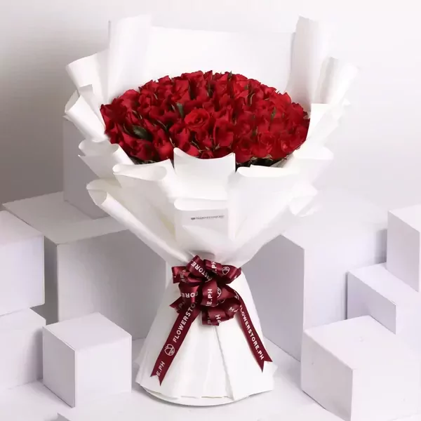 A large bouquet of 99 red roses wrapped in white paper with a maroon ribbon.