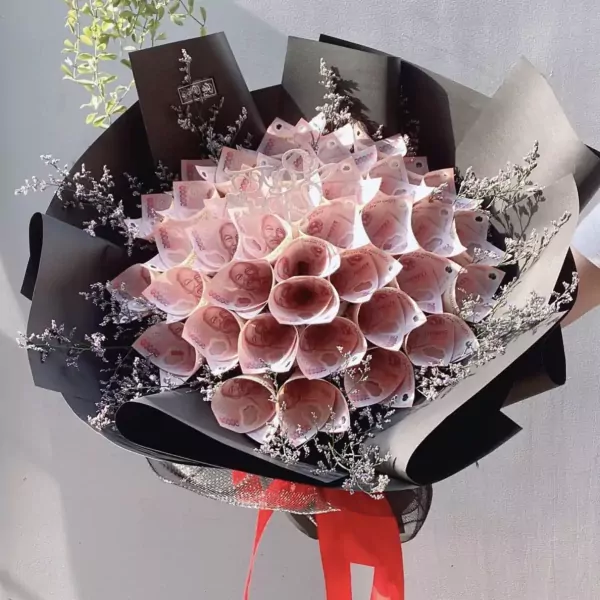 A money bouquet with rolled pink banknotes, black and grey paper, and dried baby's breath.