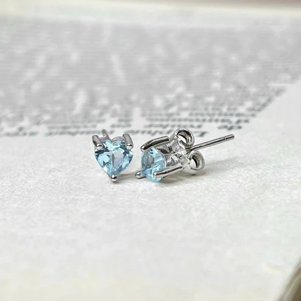 Silver heart-shaped blue topaz stud earrings on a textured background.