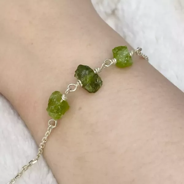 Silver bracelet with raw green peridot stones on a wrist.